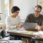Two small-business teammates vet personalized outreach lines over index cards and blurred printouts at a sunlit wooden table.