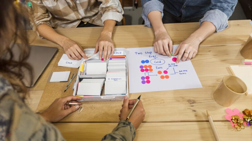 Progressive Enrichment Prospecting Workflow: A 2‑Step Playbook for Building Actionable Cold Outreach Lists with Minimal Data Two-person marketing team sorting plain index cards into color-tabbed trays beside a stickered two-step outreach flow.