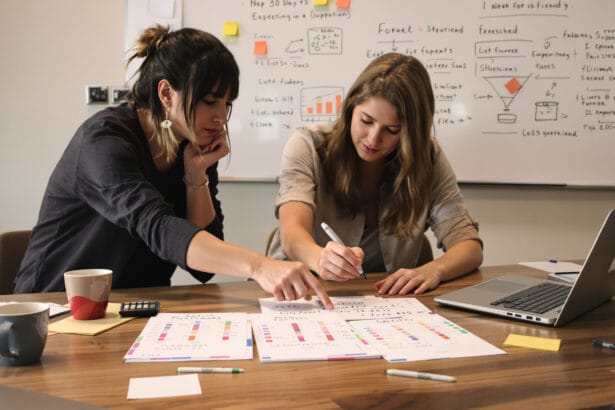 Small B2B team reviewing a blurred spreadsheet and three color-tabbed experiment card stacks at a wooden table.