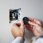 Homeowner's hands installing a tado thermostat backplate over exposed wires, removed Nest and boiler visible in background.